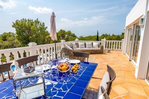 Um terraço com mesa posta para refeições, assentos externos e vista para o verde ao redor.