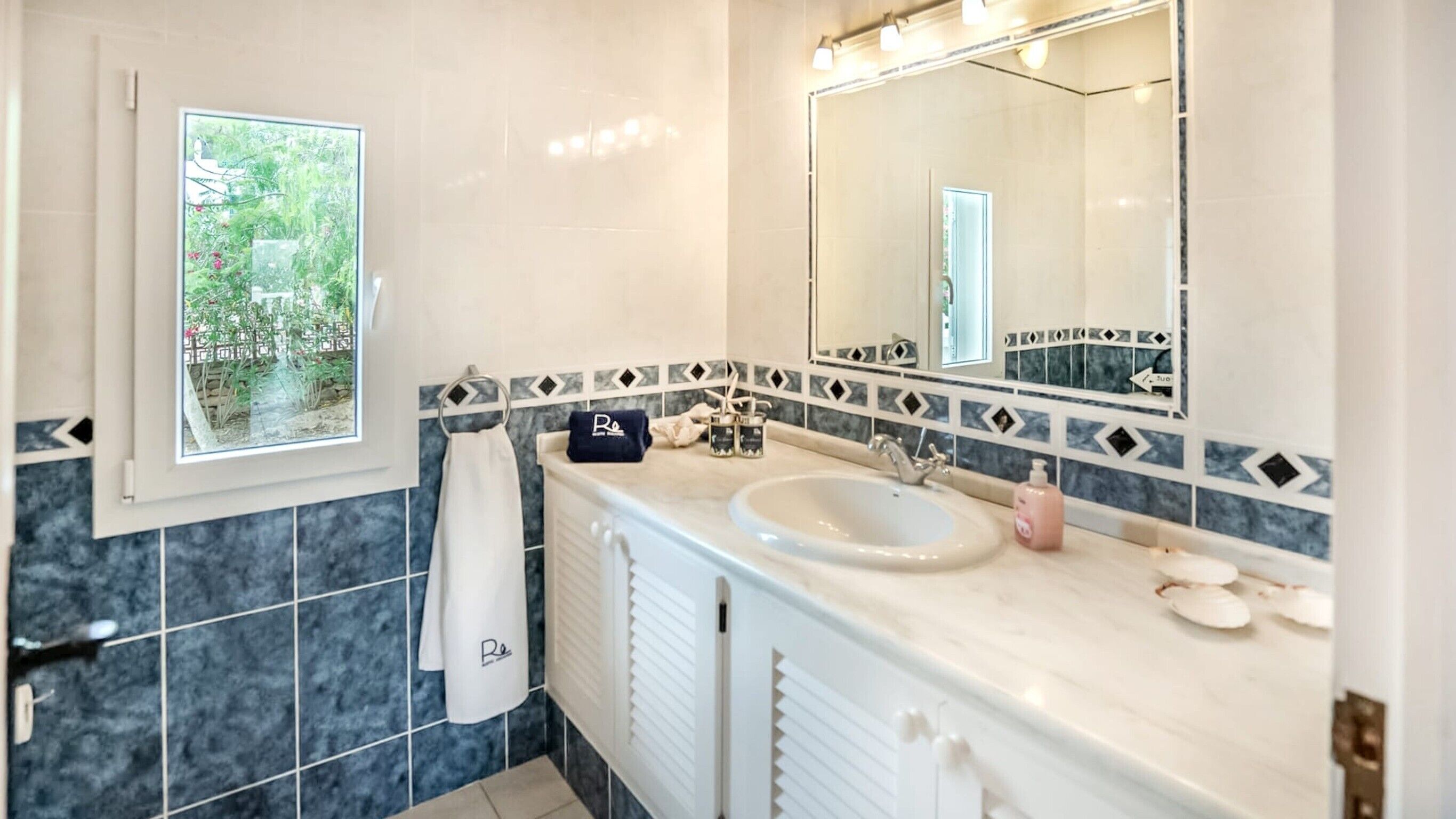 A bathroom with a large mirror, a sink, and a window with a view of greenery.