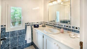 A bathroom with a large mirror, a sink, and a window with a view of greenery.