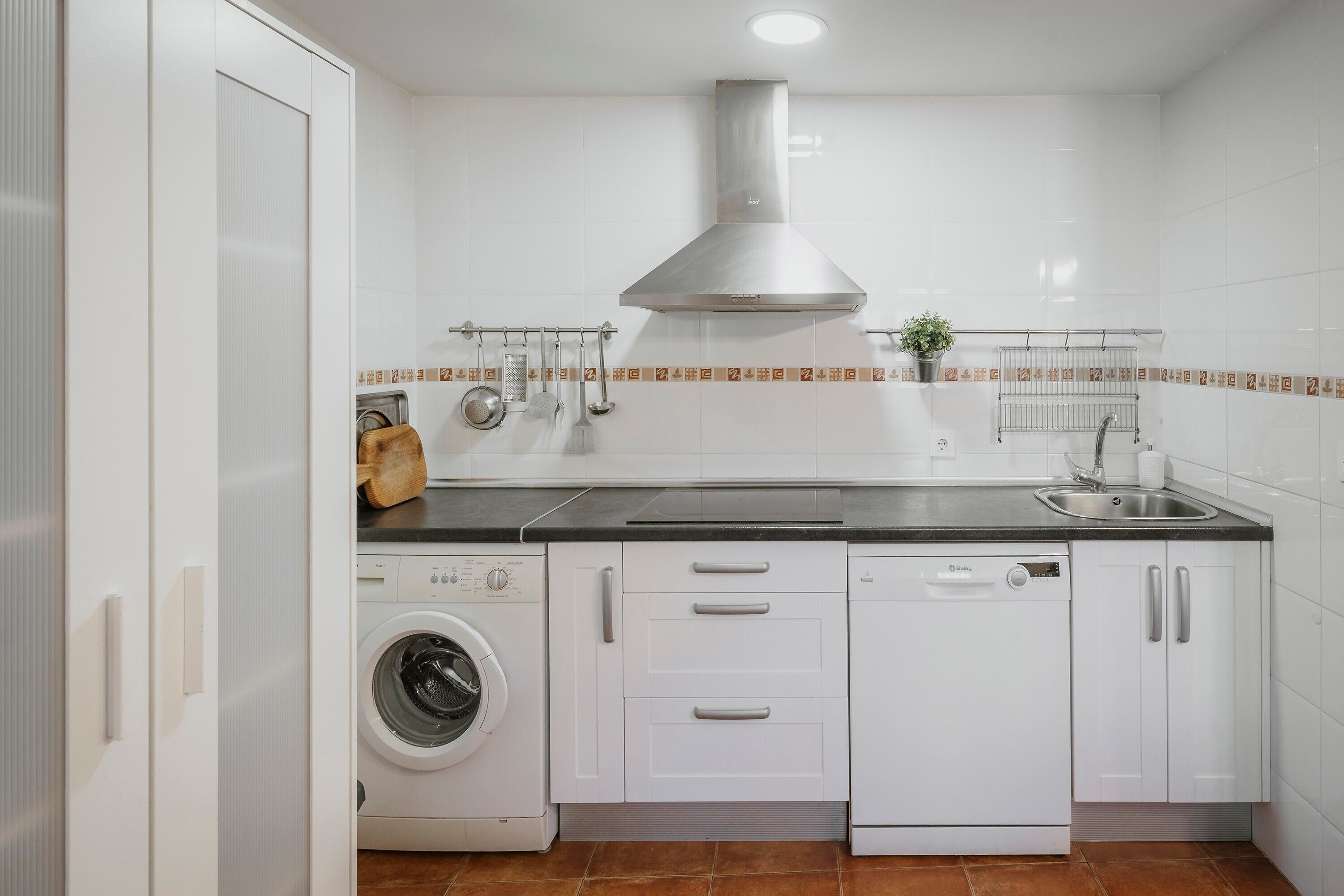 Una cocina moderna equipada con lavadora, lavavajillas y campana extractora de acero inoxidable.