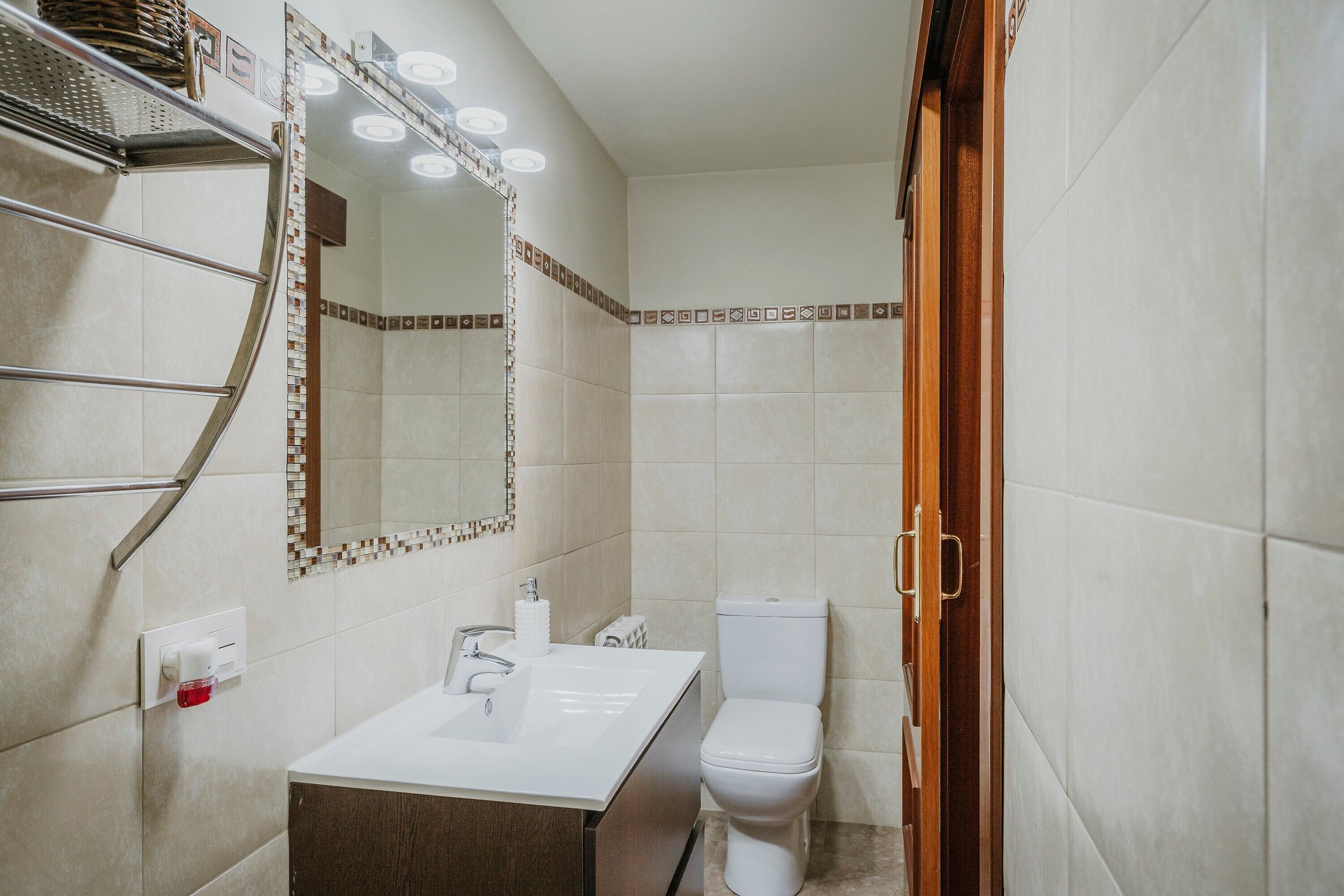 A bathroom with a white sink, a toilet, a mirror with lights, and a shower area.