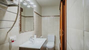A bathroom with a white sink, a toilet, a mirror with lights, and a shower area.