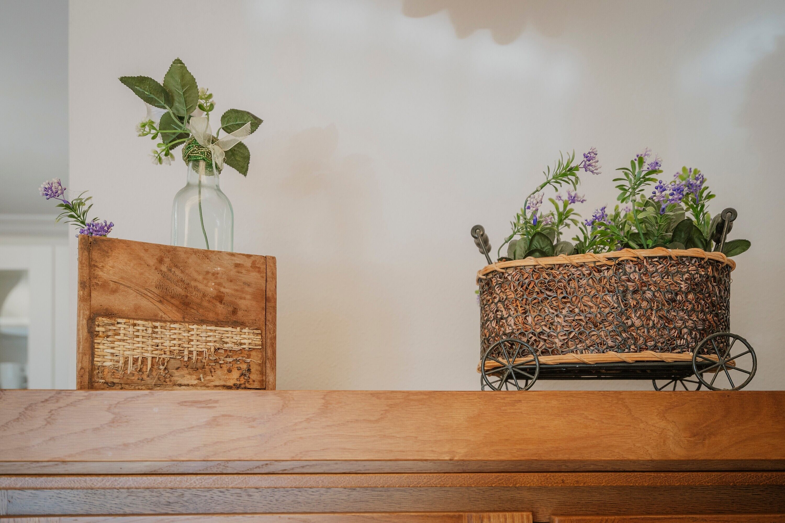 Eine Holzbank mit einem gewebten Korb und einer Glasvase mit Blumen.