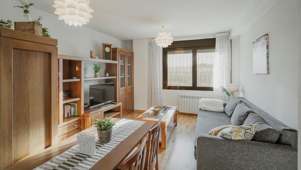 Una sala moderna con una unidad de entretenimiento de madera, un sofá, una mesa de comedor y un ventanal con cortinas.
