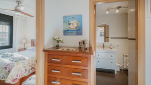 Un dormitorio con cama, cómoda de madera y baño visible a través de una puerta abierta.