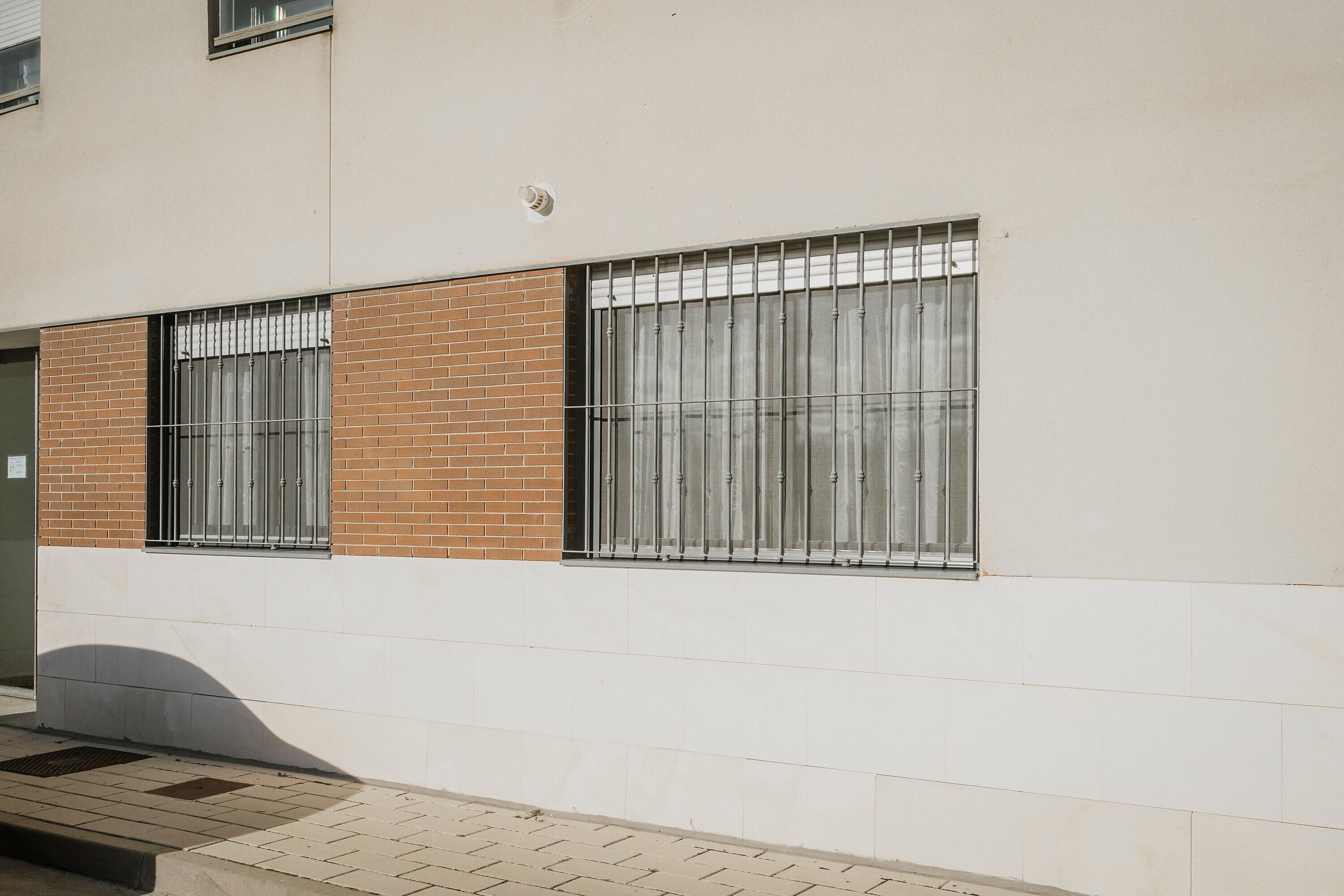 Une façade d’immeuble avec deux fenêtres, dont une avec des barreaux en métal et l’autre avec des rideaux, ainsi qu’une porte.