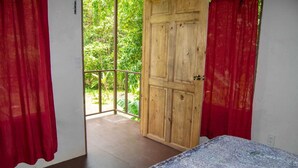 Ein Zimmer mit einem Bett, einer Holztür und einem Balkon mit Blick auf Grünflächen.