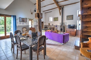 Un comedor con una mesa preparada para cuatro personas, un sofá y una televisión en una habitación rústica con vigas a la vista y chimenea.