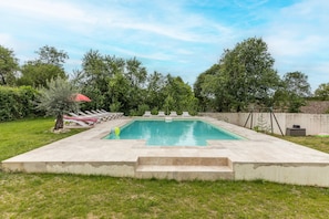 Una piscina rectangular con plataforma de hormigón, rodeada de césped y árboles.