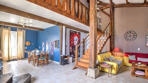 A spacious living area with a dining table, yellow sofa, and a staircase. - Magical Stay at Il était une fois Cottage – Shared Pool and Air Conditioning (Beaumontois-en-Périgord)