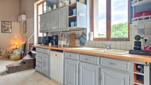 A kitchen with white cabinets, a wooden countertop, and a window with a view of greenery. - Magical Stay at Il était une fois Cottage – Shared Pool and Air Conditioning (Beaumontois-en-Périgord)