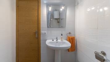 Un bany amb una porta de fusta, un lavabo blanc, un mirall i un suport per a tovalloles.
