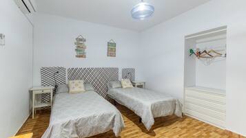 A room with two beds, a wardrobe, a bedside table, a hanging light fixture, and wall decorations.