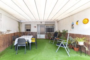 A patio with a table and chairs, a small garden area with potted plants, and a decorative sun on the wall.