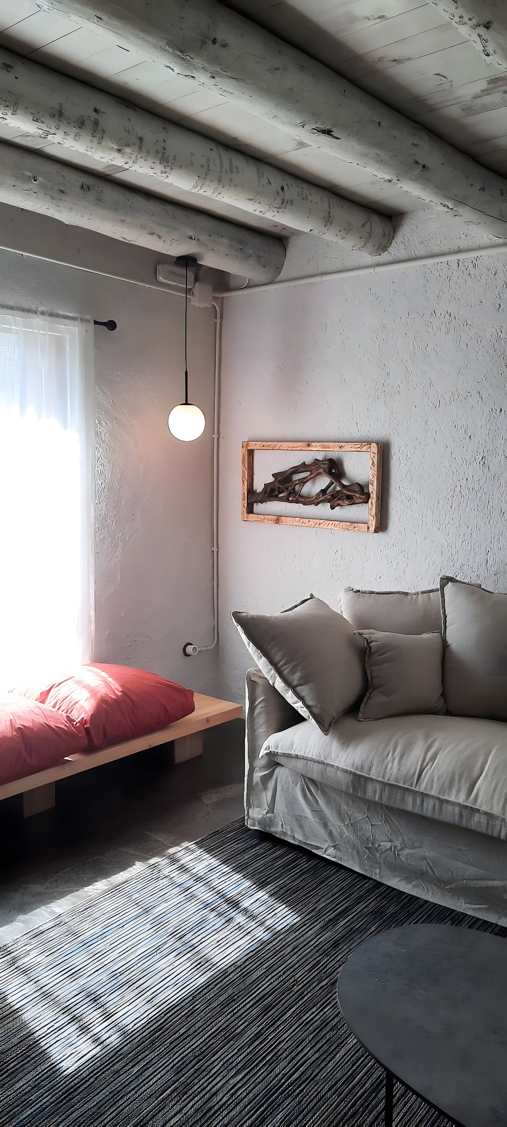Een kamer met een bed, een slaapbank, een hanglamp en een aan de muur bevestigd schilderij.