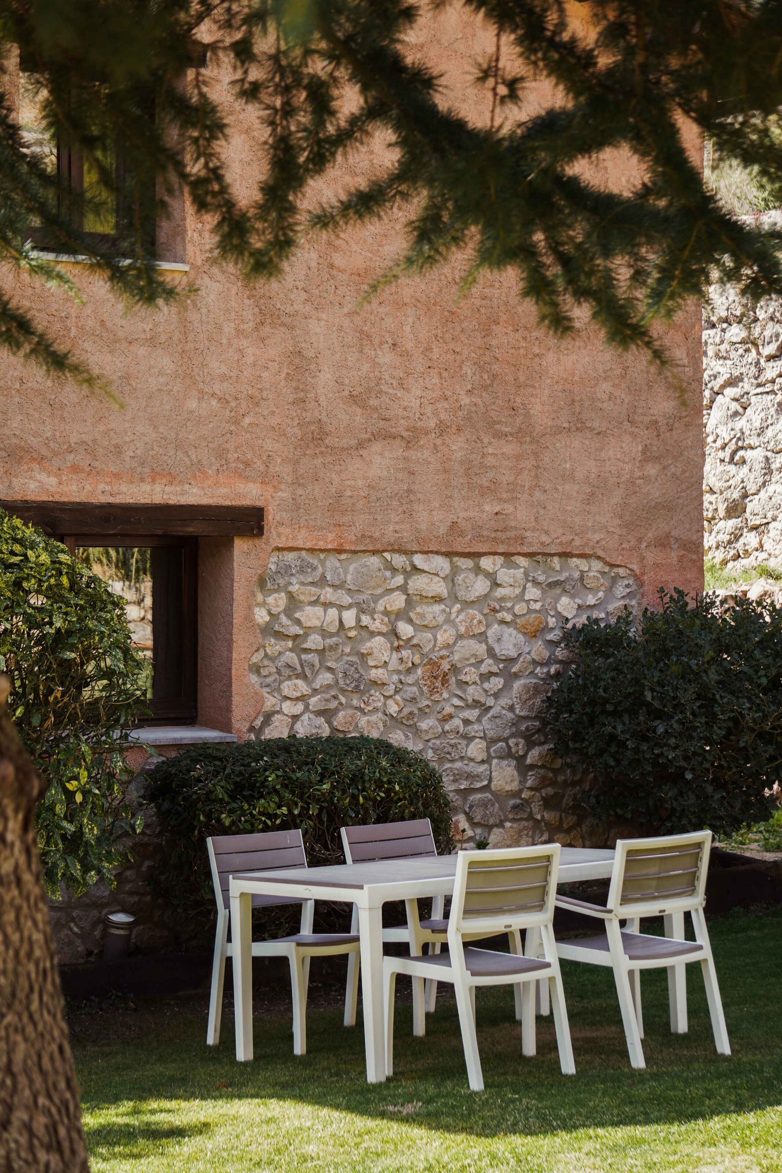 A patio with a table and chairs, a stone wall, and a building with a window.