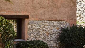A patio with a table and chairs, a stone wall, and a building with a window.