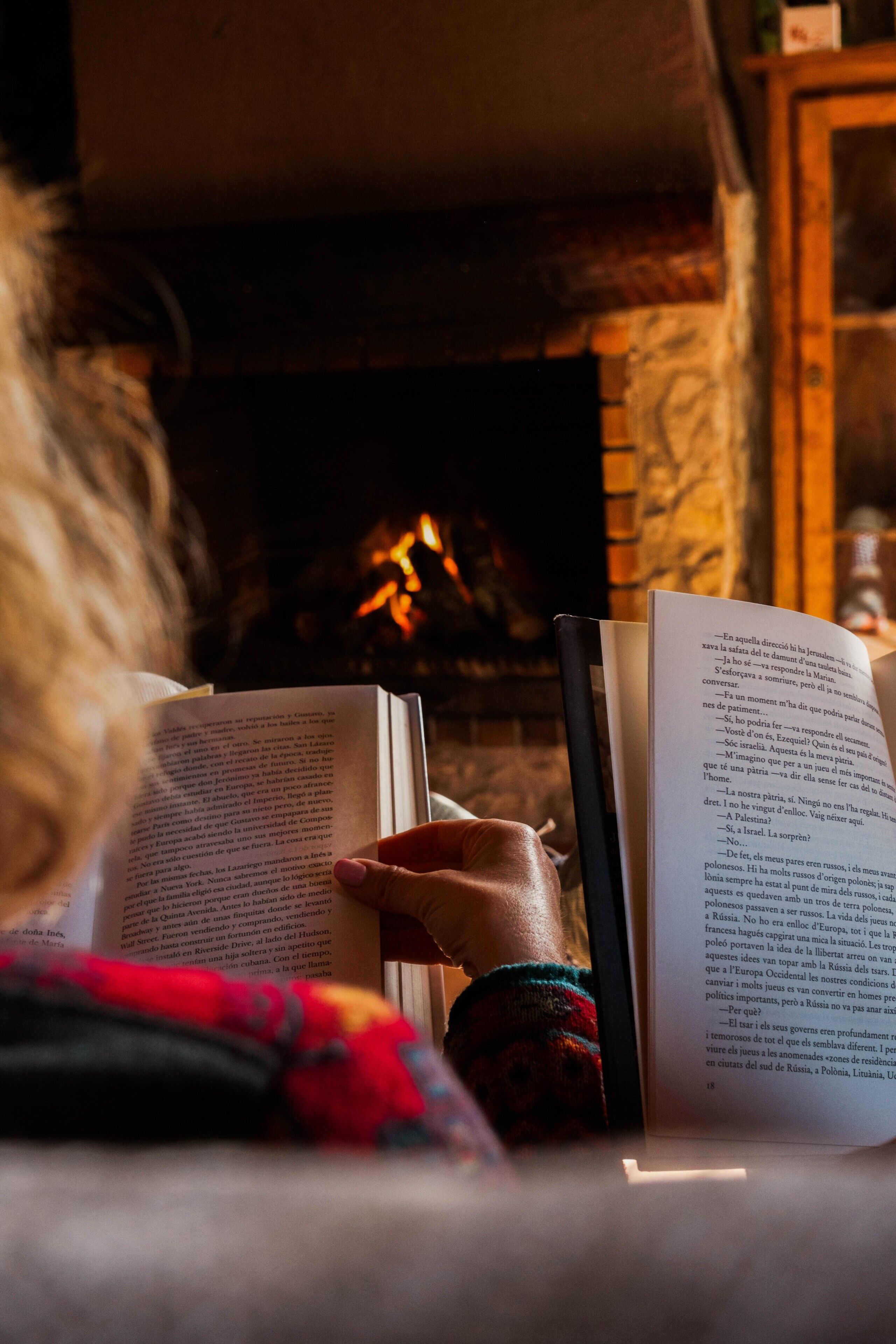 Una persona leyendo un libro junto a la chimenea.