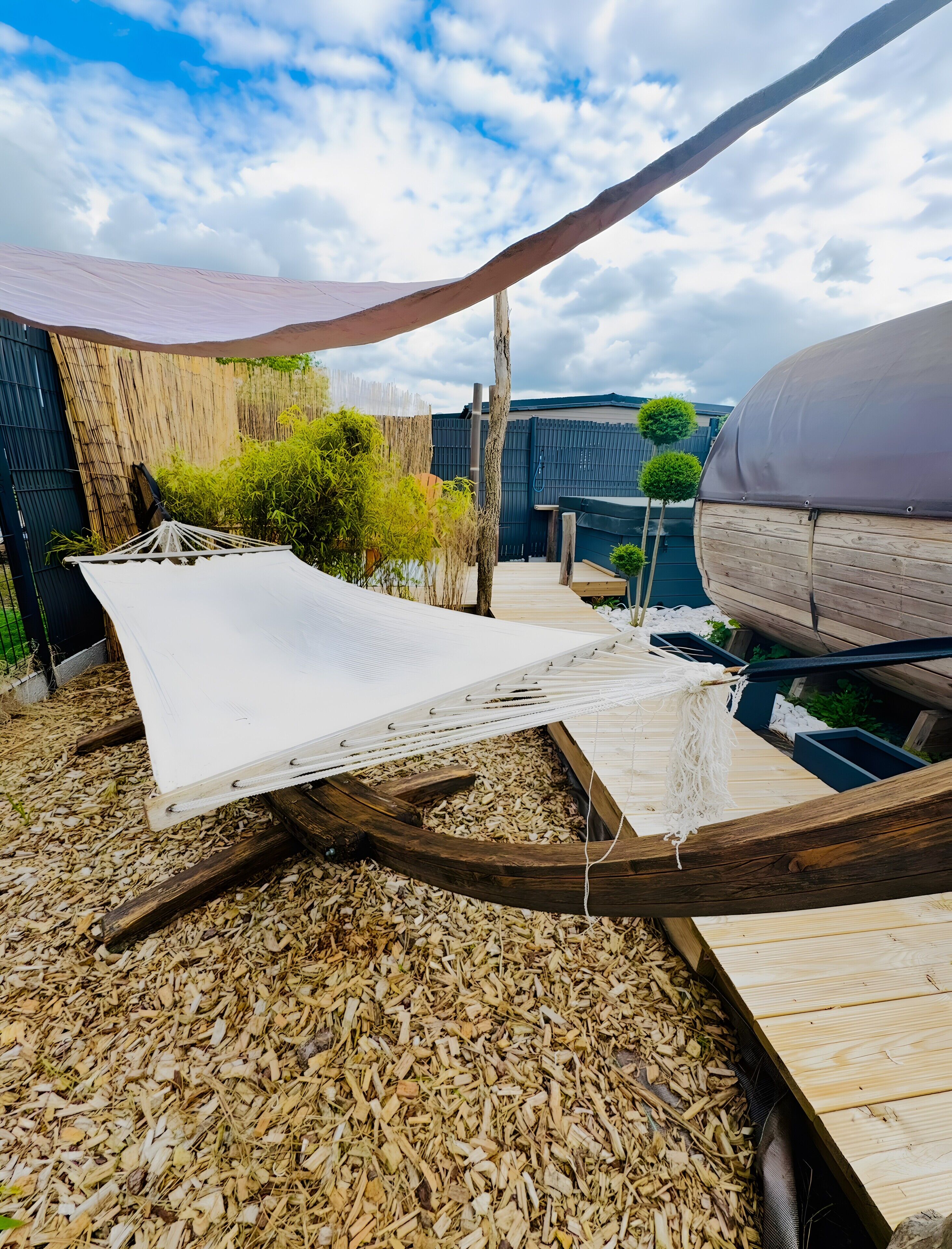A hammock, wooden deck, and a covered area in a backyard setting.
