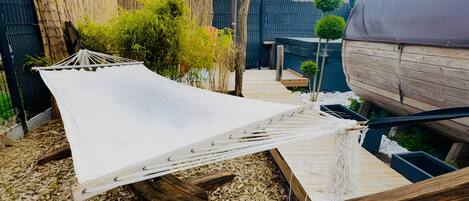 A hammock, wooden deck, and a covered area in a backyard setting.
