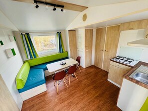 A compact kitchen with a built-in stove, wooden cabinets, a dining area with a bench and chairs, and a window with curtains.