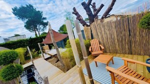 Una terraza de madera con una hamaca, una silla y una mesita.
