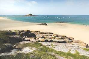 A beach with clear water, a rocky foreground, and a distant island.