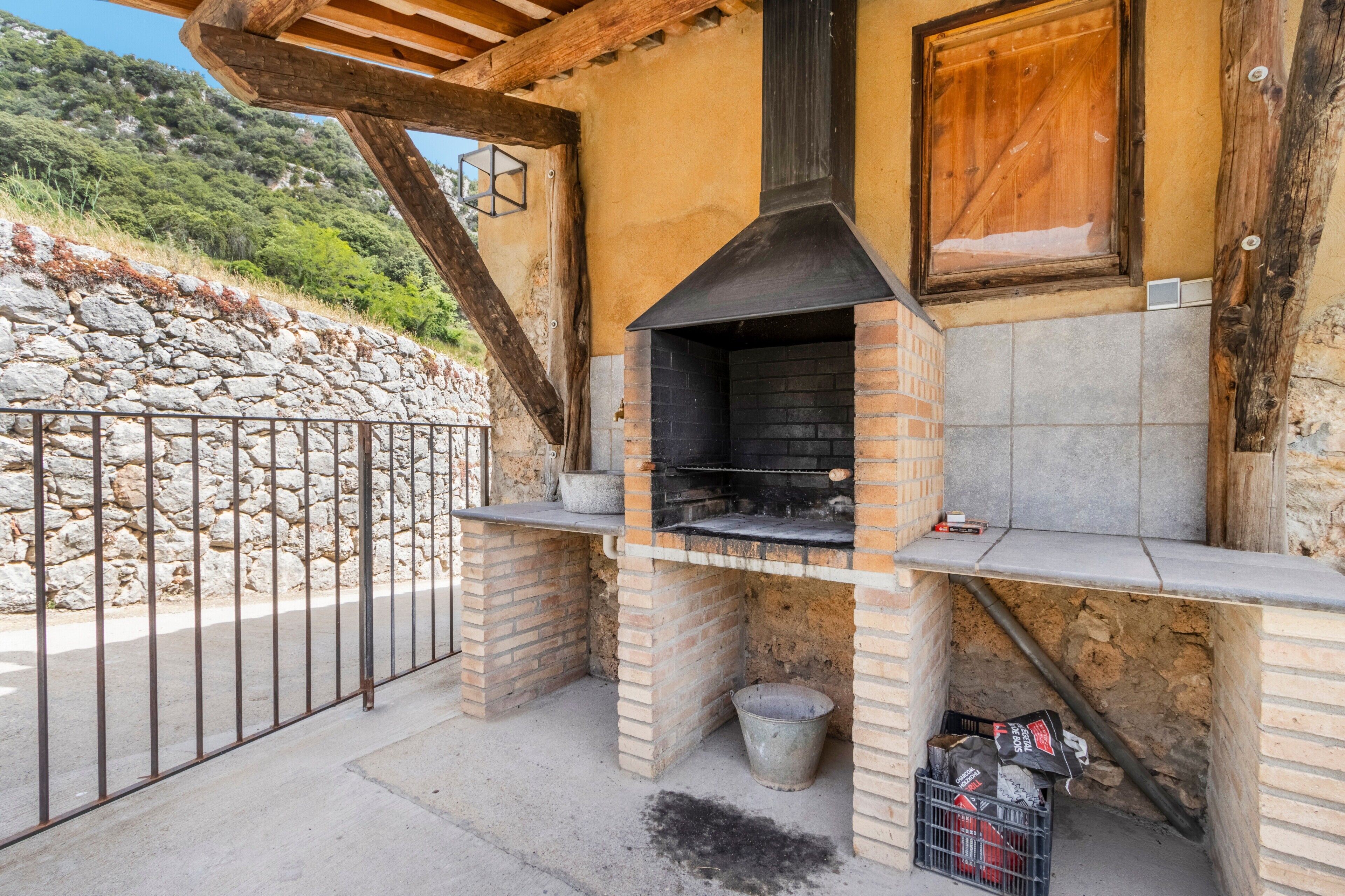 Forno in mattoni all'aperto con parete di pietra a fare da sfondo, recinzione in metallo e struttura in legno.