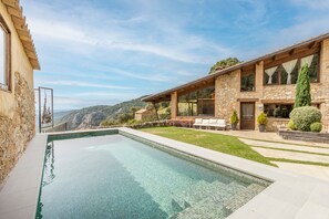 Ein modernes Haus mit Swimmingpool, Natursteinfassade und Blick auf die Hügel.