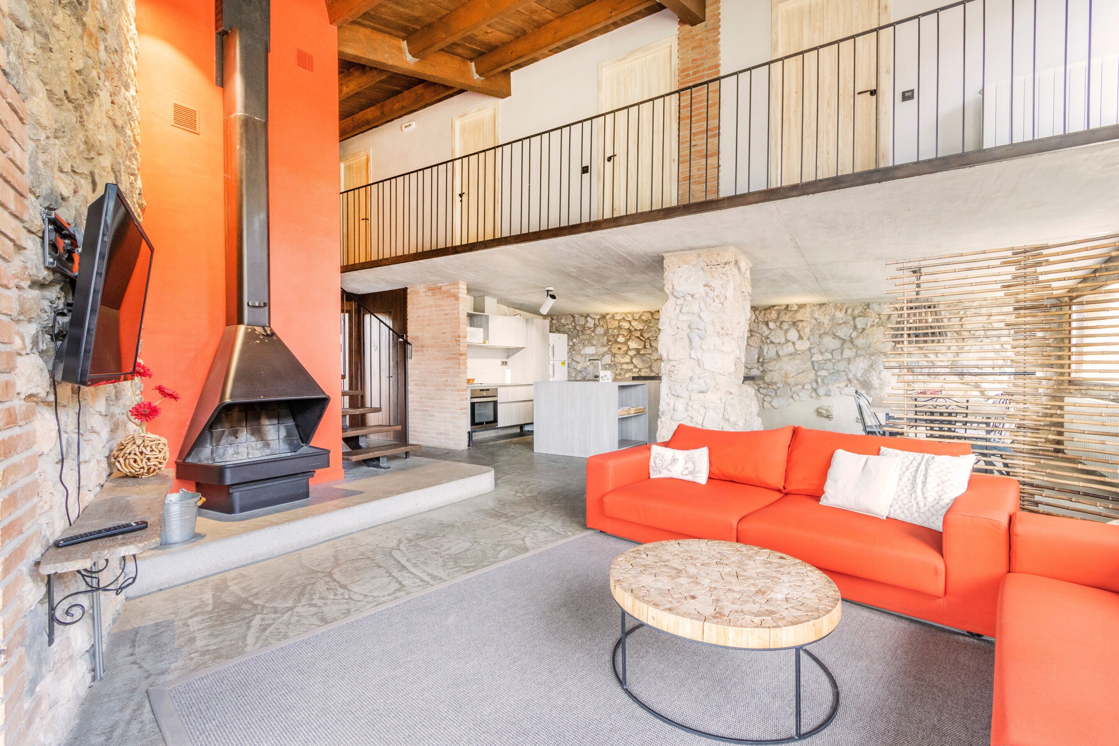 Un amplio salón con chimenea, sofá naranja y una mesa de centro redonda de madera.