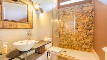 Een badkamer met een stenen muur, een witte wastafel, een toilet en een douche met glazen wanden.