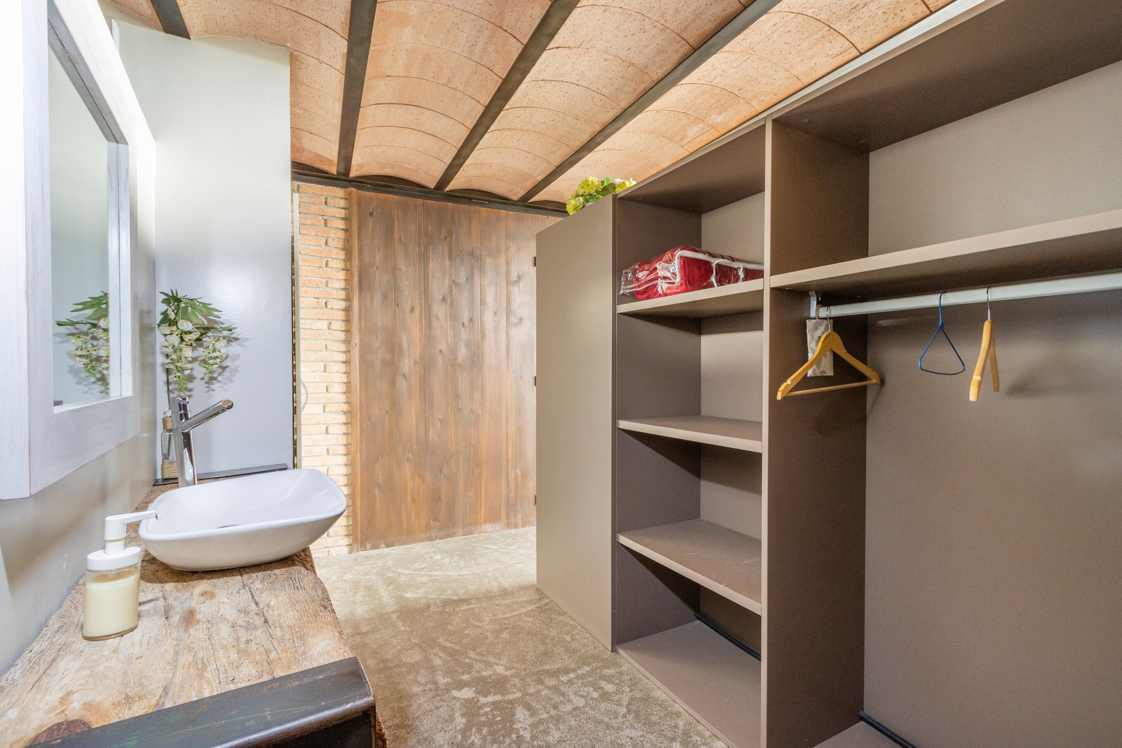 A modern bathroom with a white sink, a wooden vanity, and a walk-in closet with shelves and hangers.