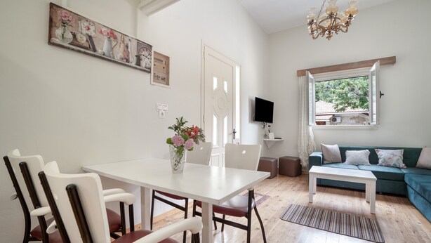 A dining area with a white table and chairs, a sofa, a TV, and a window with a view.