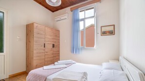 A bedroom with a bed, a wooden wardrobe, a window with curtains, and an air conditioning unit.