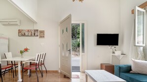 A living room with a white table, red chairs, a teal sofa, a flat-screen TV, and a door leading outside.