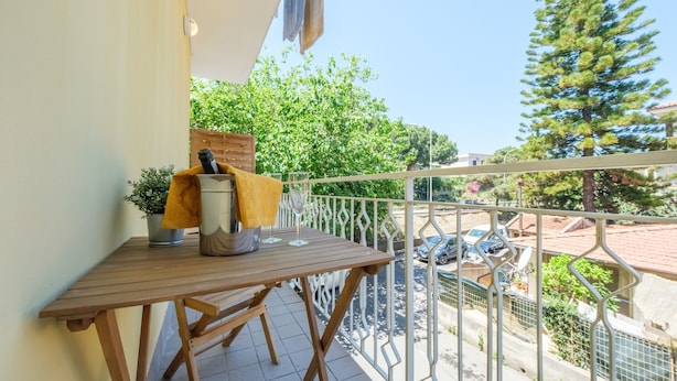 Een balkon met een houten tafel, een metalen bak en een gele doek.