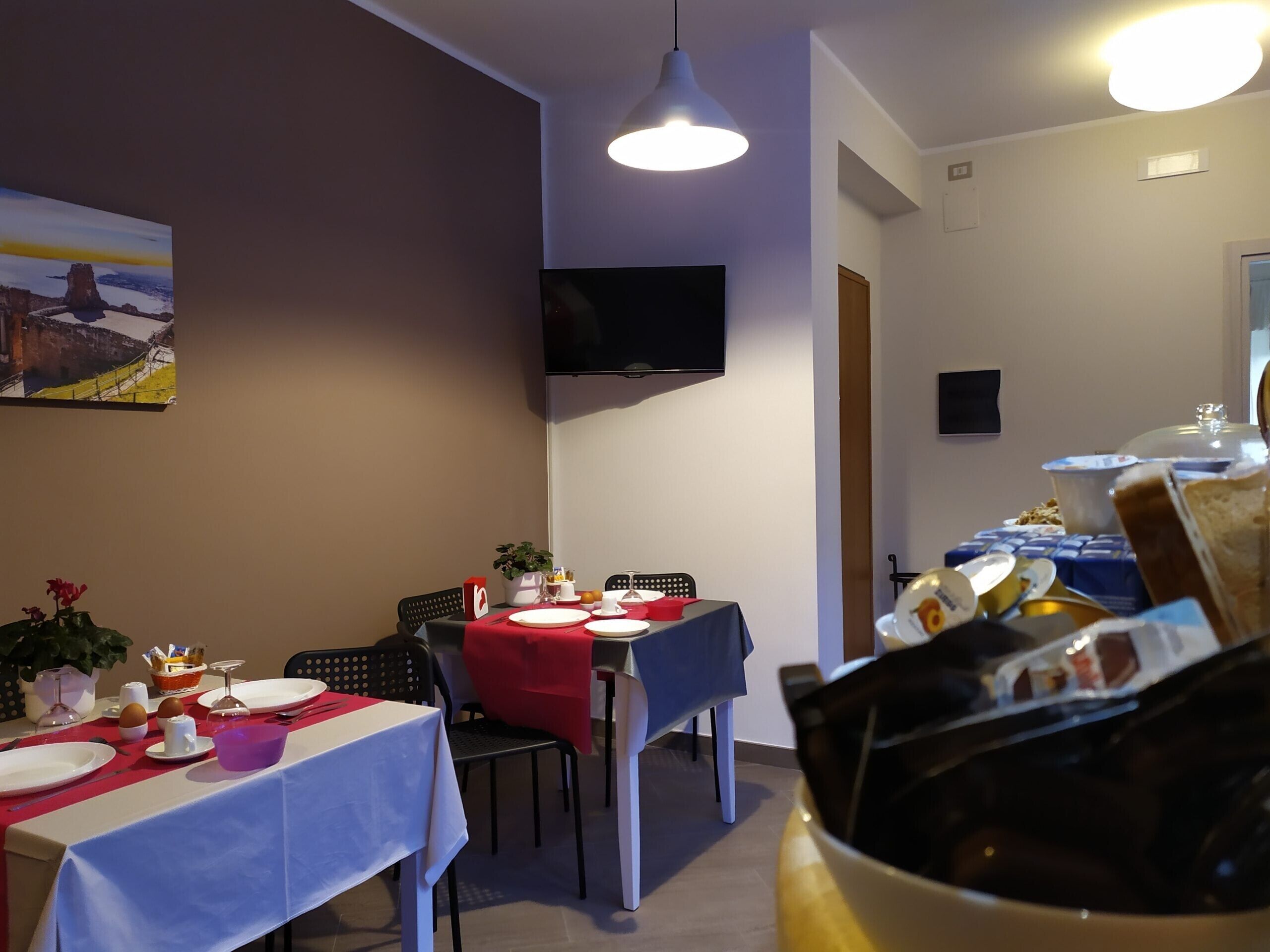 A dining area with tables set for breakfast, a flat-screen TV mounted on the wall, and a painting on the wall.
