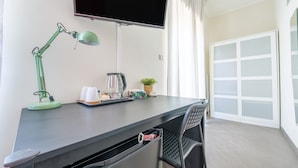 A modern room with a desk, a green desk lamp, a flat-screen TV, a potted plant, and a sliding glass door. - Room 'Taormina' with Balcony, Wi-Fi and Air Conditioning (Giardini Naxos)
