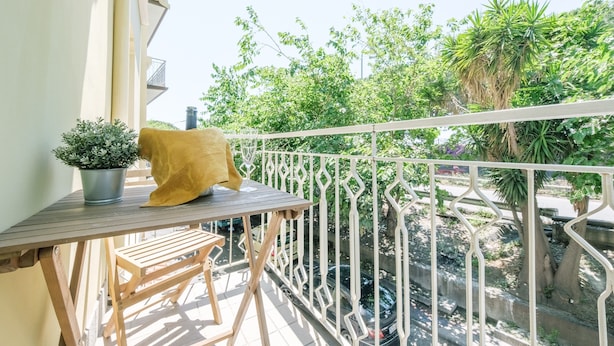 A balcony with a table, a potted plant, and a yellow cushion. - Room 'Taormina' with Balcony, Wi-Fi and Air Conditioning (Giardini Naxos)