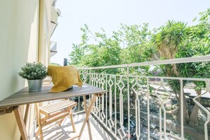 Un balcone con un tavolo, una pianta in vaso e un cuscino giallo.