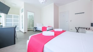 A hotel room with a bed, a desk, a chair, a TV, and a door. - Room 'Taormina' with Balcony, Wi-Fi and Air Conditioning (Giardini Naxos)