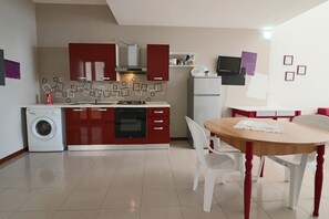 A compact kitchen with a washing machine, a dining table with chairs, and a TV mounted on the wall.