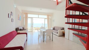 Un salon moderne avec un escalier en colimaçon rouge, des meubles blancs et une vue sur l’extérieur.