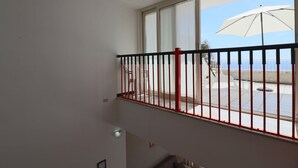 Un balcon avec une balustrade rouge, un parasol blanc et une vue sur la mer.