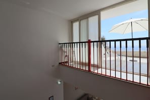 Un balcon avec une balustrade rouge, un parasol blanc et une vue sur la mer.
