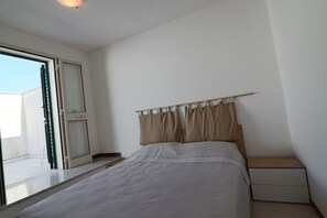 A bedroom with a bed, a nightstand, a window with curtains, and a sliding glass door.