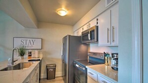 A modern kitchen with stainless steel appliances, a microwave, and a coffee maker. There is a trash can and a framed sign on the wall. - Lakefront Condo on Lake Conroe at The Lodge. (Montgomery)