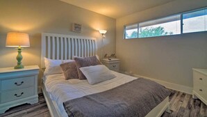 A bedroom with a bed, a nightstand, a lamp, a bedside table, and a window with blinds. - Lakefront Condo on Lake Conroe at The Lodge. (Montgomery)