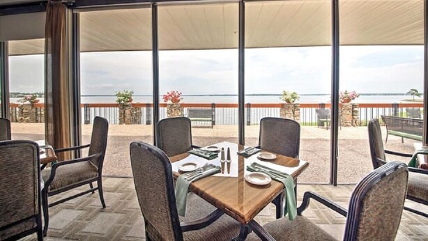 A dining area with a table set for four, large windows with a view of the sea, and a covered outdoor seating area. - Lakefront Condo on Lake Conroe at The Lodge. (Montgomery)