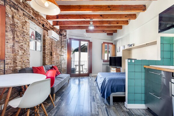 Une pièce avec un mur en briques, des poutres apparentes, une table à manger avec des chaises, un canapé, un lit et un coin cuisine.